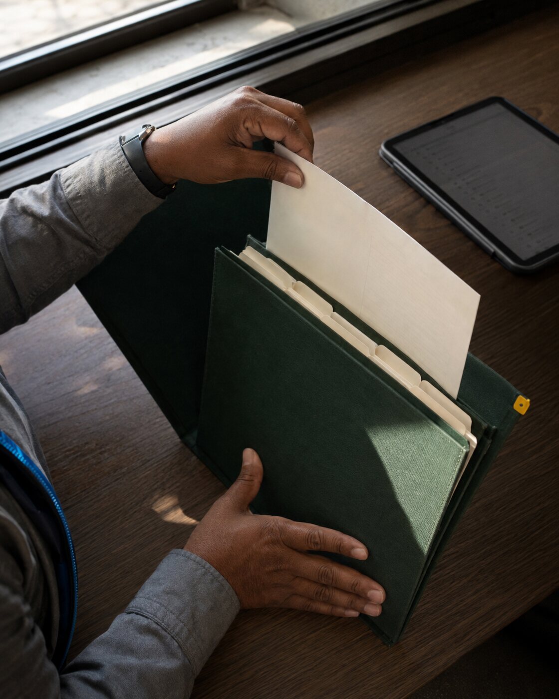 Hands organize a tabbed paper file beside a tablet.